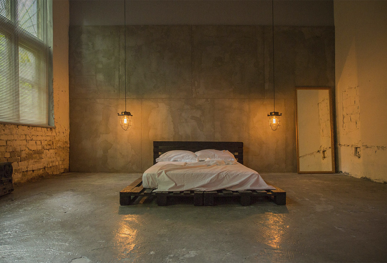 Зона Bedroom в павільйоні лофт: ліжко на дерев'яних палетах на фоні бетонної стіни | Оренда студії для зйомки фото